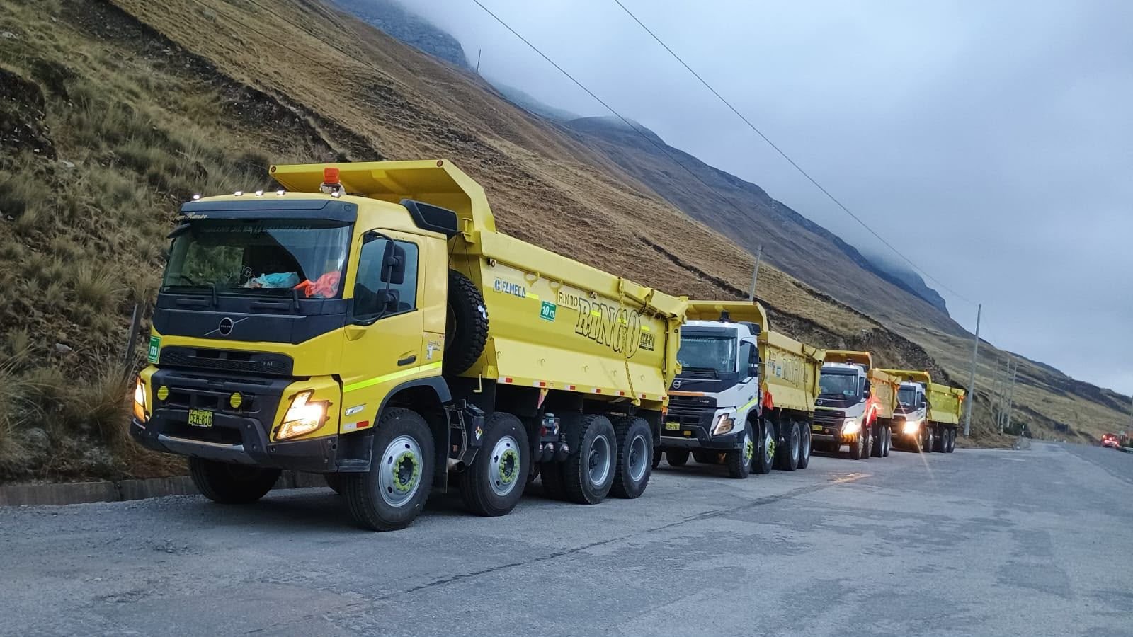 Flota de volquetes Ringo estacionados en fila en una carretera de montaña con neblina.